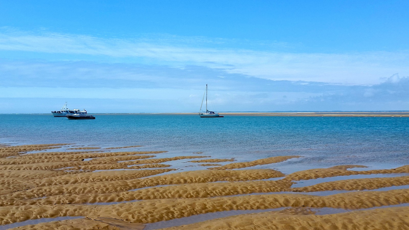 tide out on a golden sandy beach with a boat on the blue water